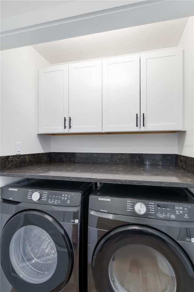 clothes washing area featuring washing machine and dryer and cabinets