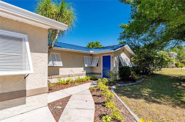 view of exterior entry with metal roof, a yard, a standing seam roof, and stucco siding