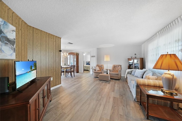 living room featuring a textured ceiling, wooden walls, a chandelier, and light wood-type flooring