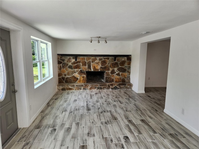 unfurnished living room with track lighting, a stone fireplace, and light hardwood / wood-style flooring