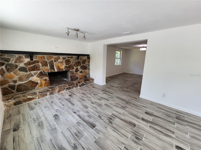 unfurnished living room with rail lighting, a stone fireplace, and light hardwood / wood-style floors