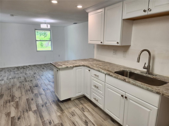 kitchen featuring light stone countertops, sink, white cabinets, and kitchen peninsula