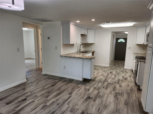 kitchen featuring hardwood / wood-style floors, sink, white cabinets, light stone counters, and kitchen peninsula