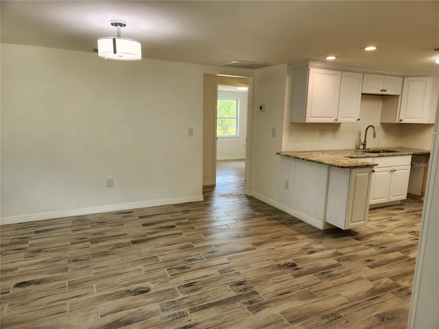 kitchen with pendant lighting, sink, wood-type flooring, light stone countertops, and white cabinets