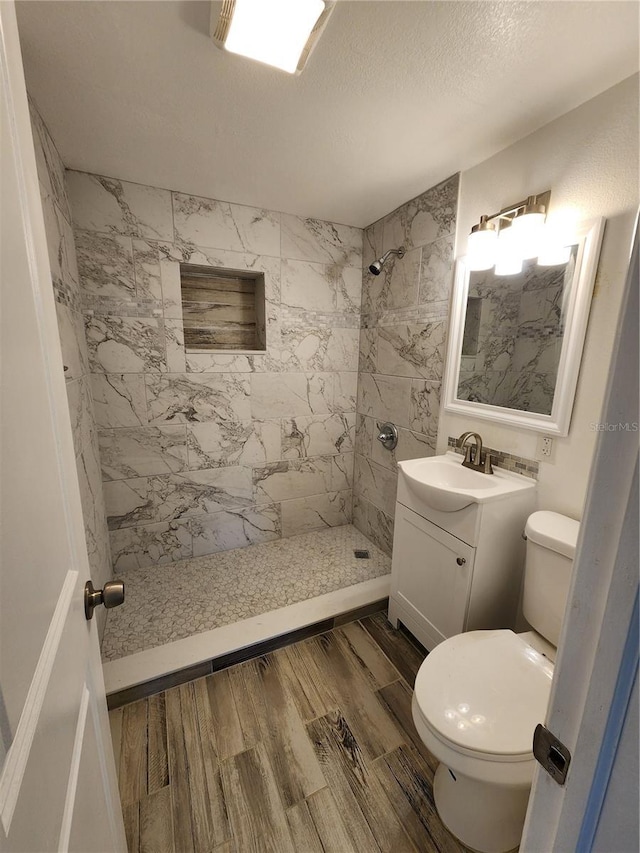 bathroom with tiled shower, vanity, toilet, and a textured ceiling