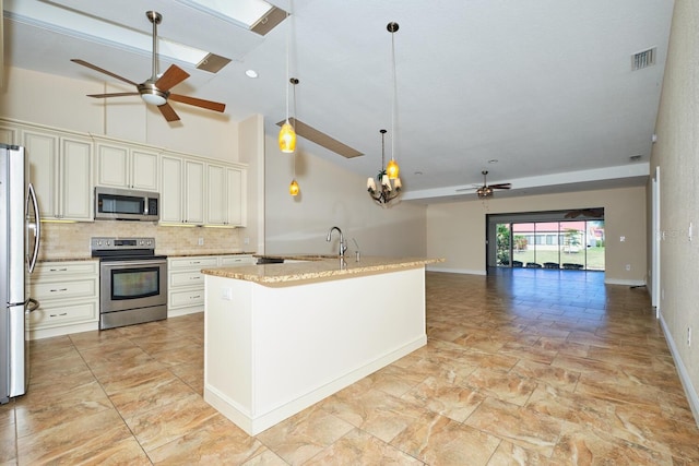 kitchen with appliances with stainless steel finishes, pendant lighting, an island with sink, decorative backsplash, and light stone countertops