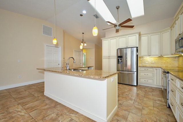 kitchen featuring appliances with stainless steel finishes, cream cabinets, an island with sink, sink, and light stone countertops