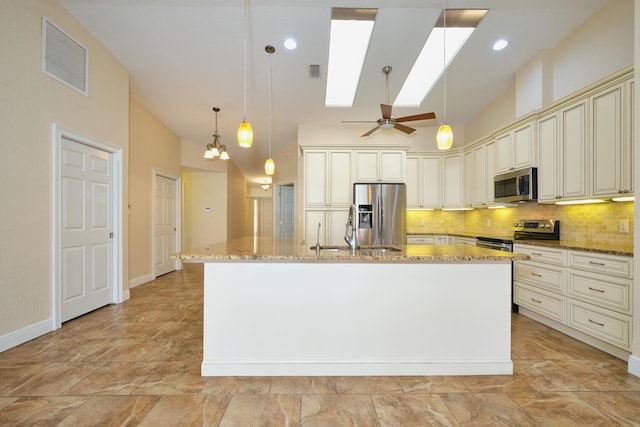 kitchen with light stone counters, appliances with stainless steel finishes, an island with sink, and cream cabinetry