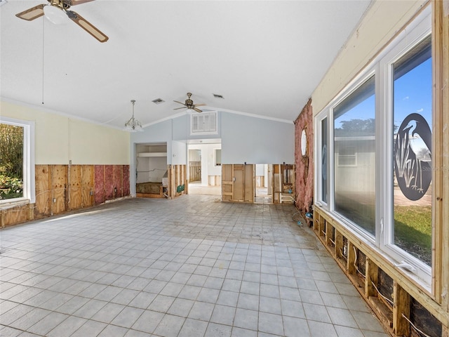 unfurnished living room featuring a healthy amount of sunlight, lofted ceiling, ceiling fan with notable chandelier, and wood walls