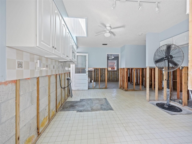 interior space with a textured ceiling, track lighting, and ceiling fan