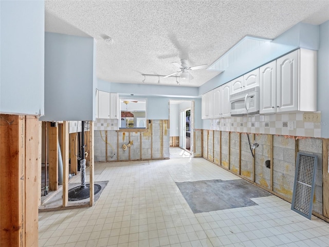 kitchen featuring white cabinetry, ceiling fan, tile walls, and a textured ceiling