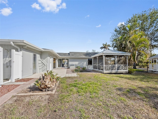 rear view of property featuring a patio, a sunroom, and a lawn