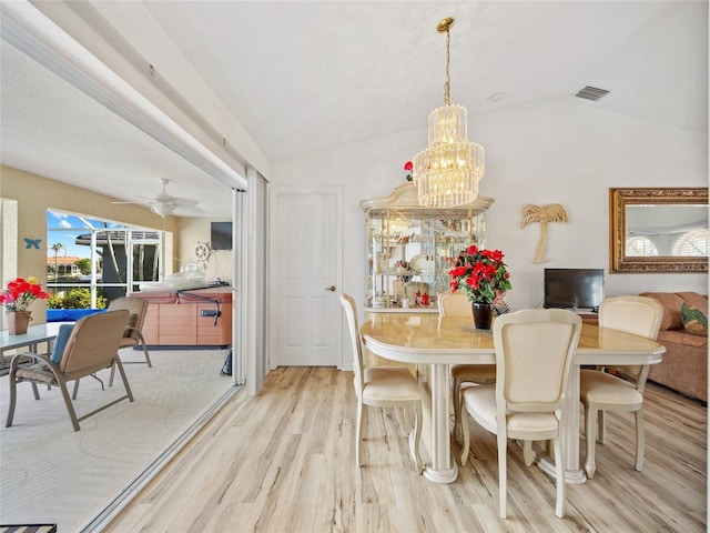 dining room with vaulted ceiling, ceiling fan with notable chandelier, and light hardwood / wood-style flooring