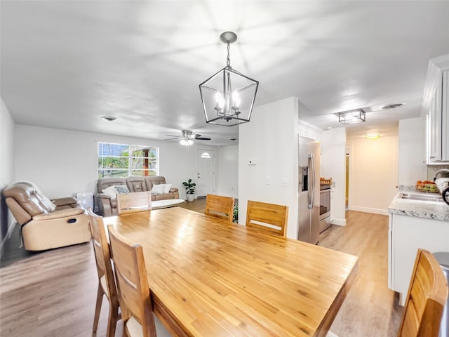 dining room featuring ceiling fan with notable chandelier, sink, and light wood-type flooring