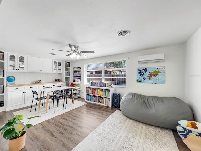 living room with hardwood / wood-style floors, a wall unit AC, and ceiling fan