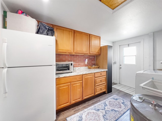 kitchen with hardwood / wood-style flooring, white refrigerator, light stone countertops, decorative backsplash, and washer / dryer