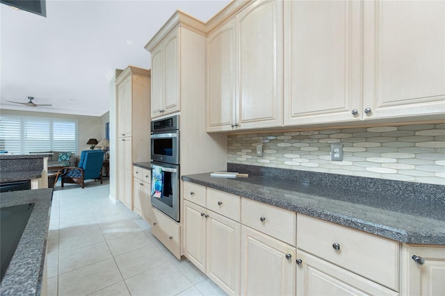 kitchen with light tile patterned floors, dark stone countertops, double oven, ceiling fan, and decorative backsplash