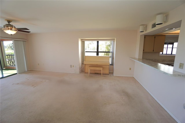 unfurnished living room with light carpet, a wealth of natural light, and ceiling fan