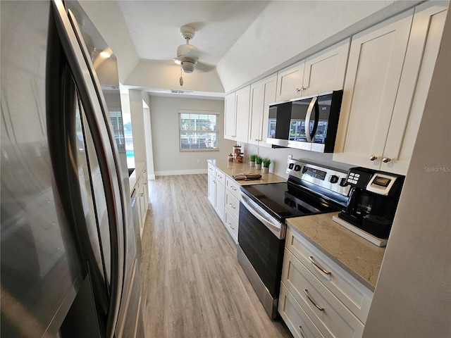 kitchen featuring lofted ceiling, appliances with stainless steel finishes, light stone counters, light hardwood / wood-style floors, and white cabinets