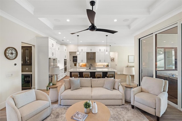 living room with sink, ceiling fan, coffered ceiling, ornamental molding, and beverage cooler