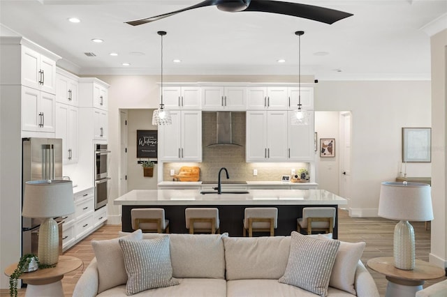 kitchen with white cabinets, a center island with sink, wall chimney exhaust hood, and decorative light fixtures