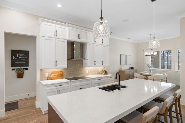 kitchen with wall chimney exhaust hood, sink, hanging light fixtures, decorative backsplash, and white cabinets