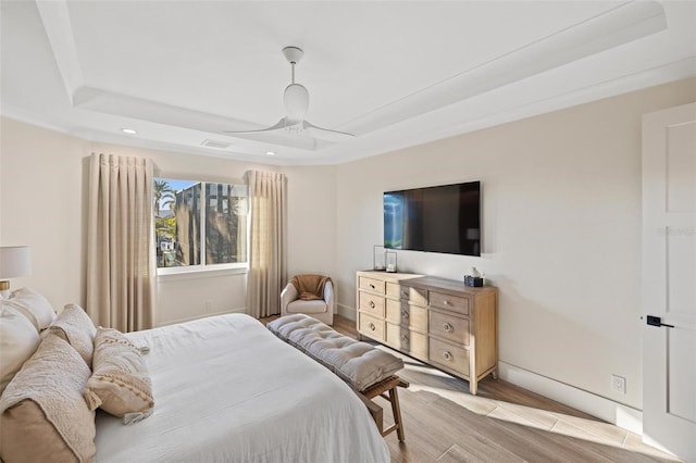 bedroom featuring ceiling fan, light wood-type flooring, and a tray ceiling