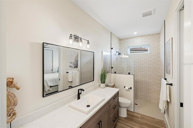 bathroom with a tile shower, vanity, and toilet