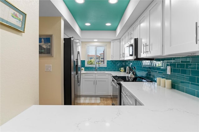 kitchen featuring sink, white cabinets, stainless steel appliances, light stone countertops, and backsplash