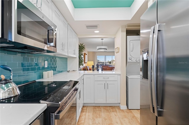 kitchen featuring stainless steel appliances, stacked washing maching and dryer, pendant lighting, and white cabinetry