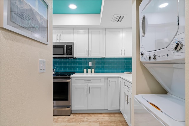 kitchen featuring light hardwood / wood-style flooring, appliances with stainless steel finishes, backsplash, stacked washer and clothes dryer, and white cabinets