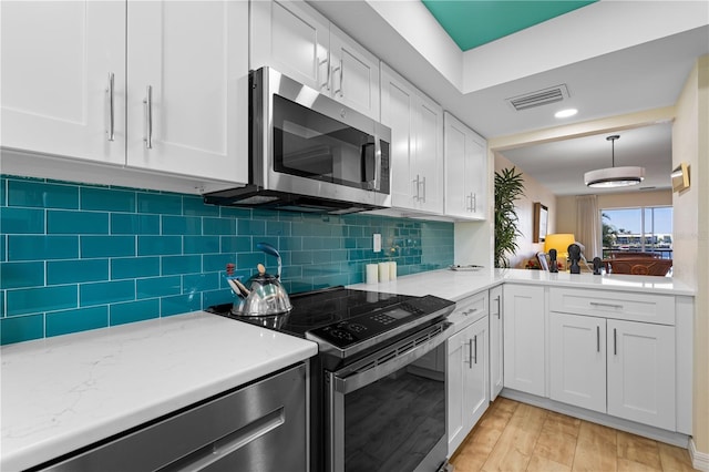 kitchen featuring appliances with stainless steel finishes, pendant lighting, tasteful backsplash, white cabinetry, and light wood-type flooring