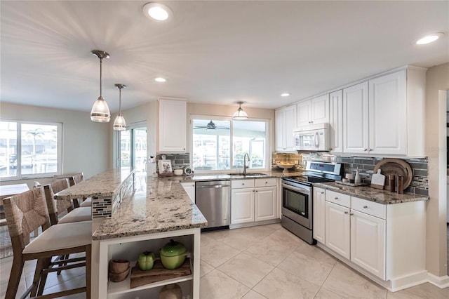 kitchen featuring stone countertops, decorative light fixtures, kitchen peninsula, stainless steel appliances, and white cabinets