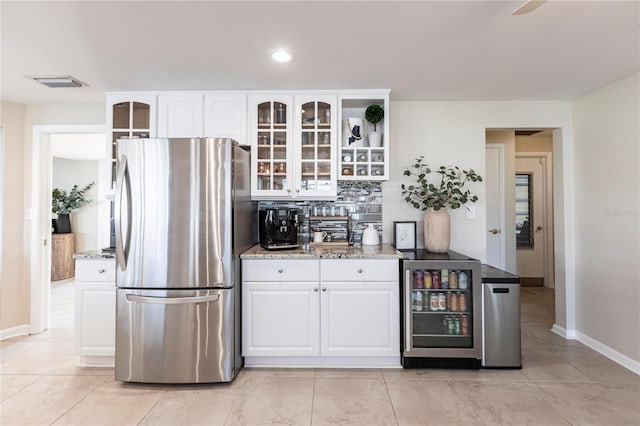 kitchen featuring light stone countertops, stainless steel refrigerator, and white cabinets