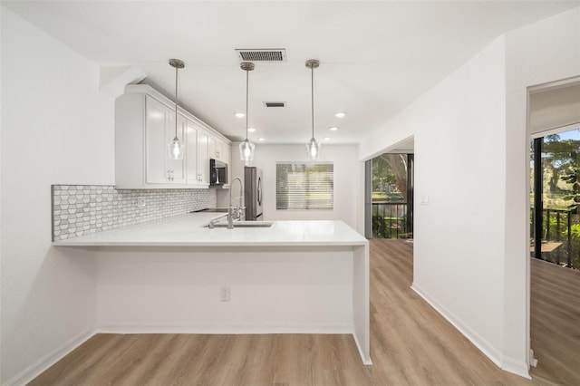 kitchen featuring pendant lighting, white cabinets, decorative backsplash, kitchen peninsula, and stainless steel appliances