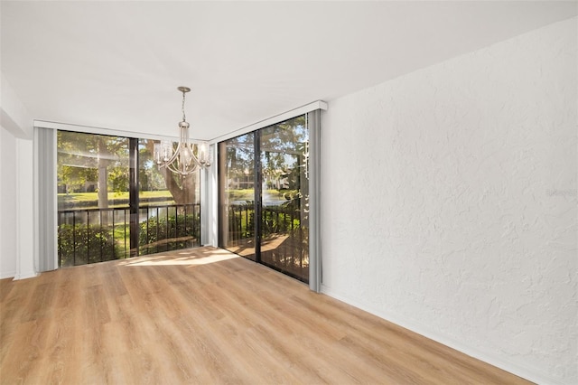 empty room featuring expansive windows, an inviting chandelier, and light hardwood / wood-style floors