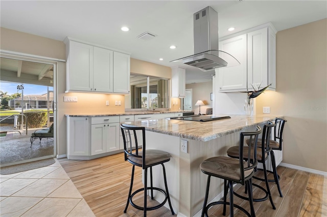 kitchen featuring black electric stovetop, white cabinetry, island range hood, a peninsula, and a kitchen bar