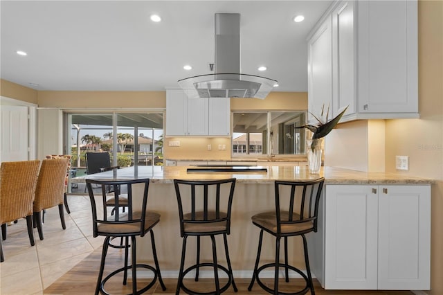 kitchen with white cabinetry, island exhaust hood, kitchen peninsula, and light stone counters