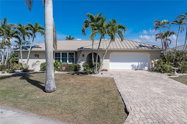 ranch-style home featuring decorative driveway, stucco siding, a standing seam roof, metal roof, and a garage