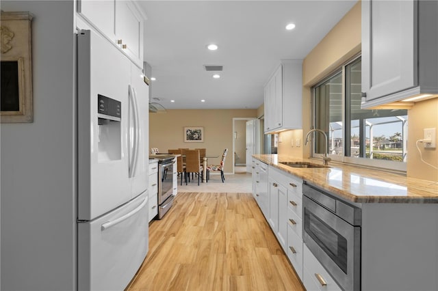 kitchen with light stone counters, white cabinetry, stainless steel appliances, and a sink