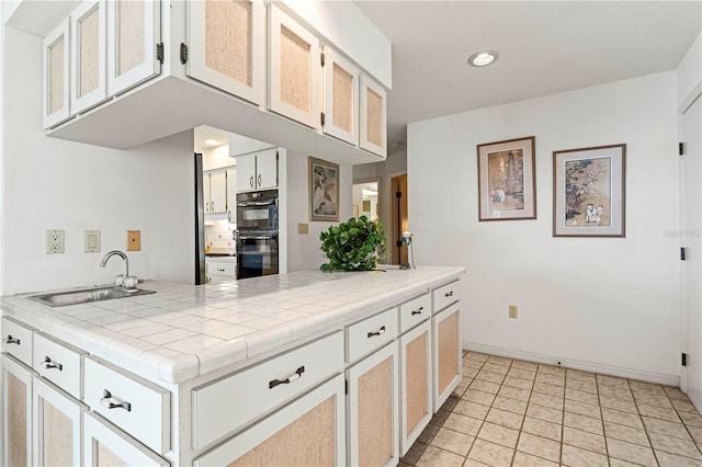 kitchen with white cabinetry, sink, tile countertops, and black double oven