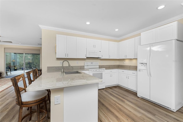 kitchen with white appliances, a breakfast bar area, a peninsula, white cabinetry, and a sink