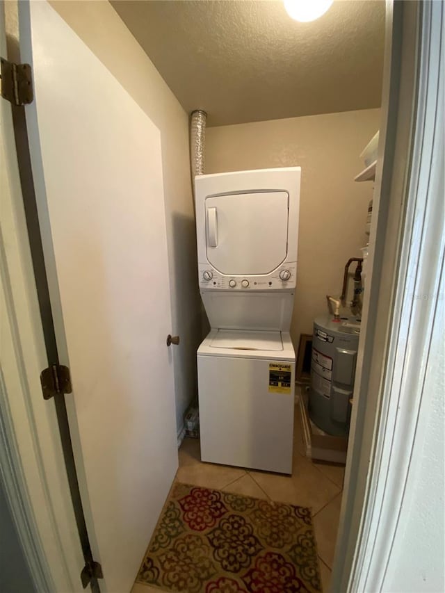 laundry area with light tile patterned floors, laundry area, stacked washer and clothes dryer, a textured ceiling, and water heater