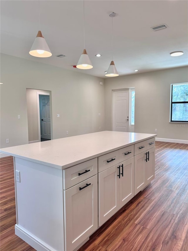 kitchen with dark wood-type flooring, hanging light fixtures, light stone countertops, white cabinets, and a kitchen island