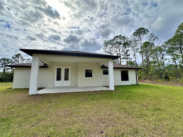 rear view of house with a patio area, a lawn, french doors, and stucco siding