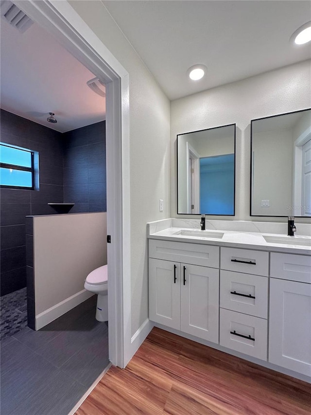 bathroom with hardwood / wood-style flooring, vanity, a tile shower, and toilet