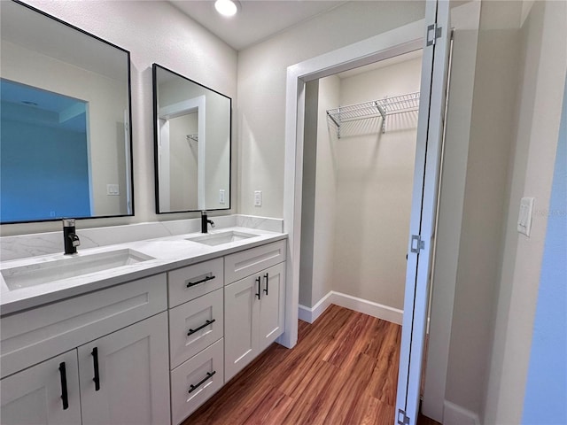 full bath with a sink, baseboards, wood finished floors, and double vanity