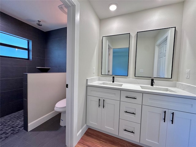 bathroom featuring hardwood / wood-style floors, vanity, a tile shower, and toilet