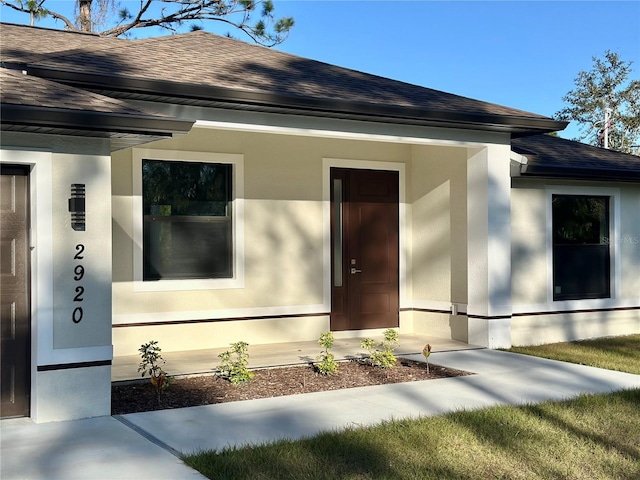 entrance to property with stucco siding and a shingled roof