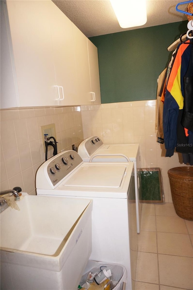 clothes washing area with light tile patterned flooring, separate washer and dryer, tile walls, cabinets, and a textured ceiling